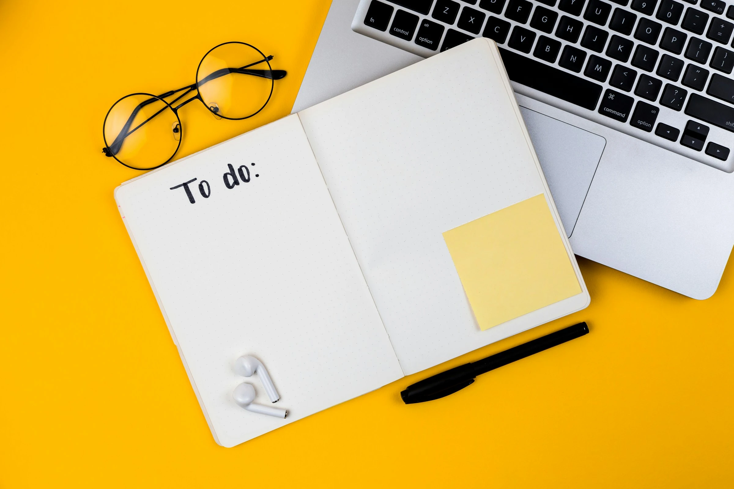 Laptop beside a to-do notebook on a yellow desk